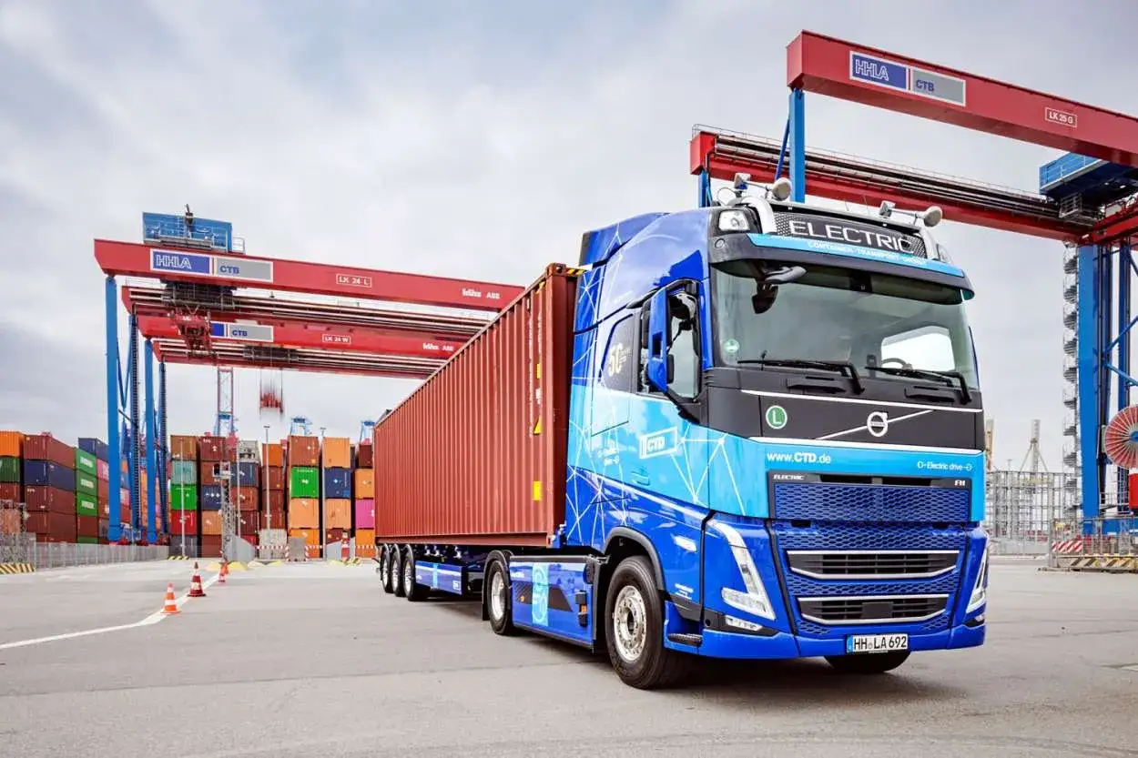Blauer Elektro-LKW mit rotem Container im Hafen, bereit zur Abholung durch den Empfänger.
