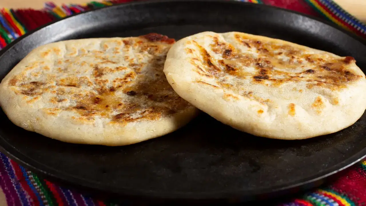 Due focacce dorate, appena cotte in padella, su un piatto nero. Il pane in padella &egrave; pronto per essere gustato.