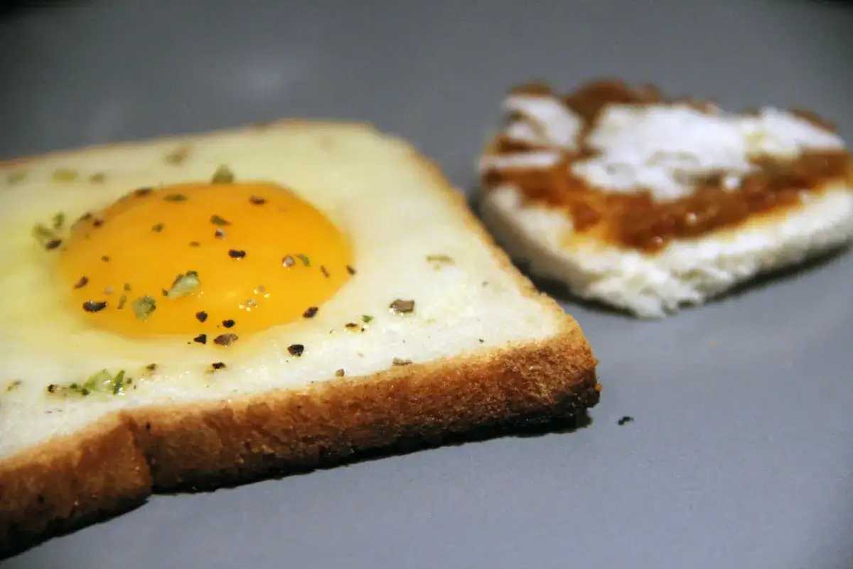 Une tranche de pain de mie avec un &oelig;uf au plat cuit &agrave; la po&ecirc;le, assaisonn&eacute; d'herbes. Une autre tranche est visible en arri&egrave;re-plan. Parfait pour une recette rapide.