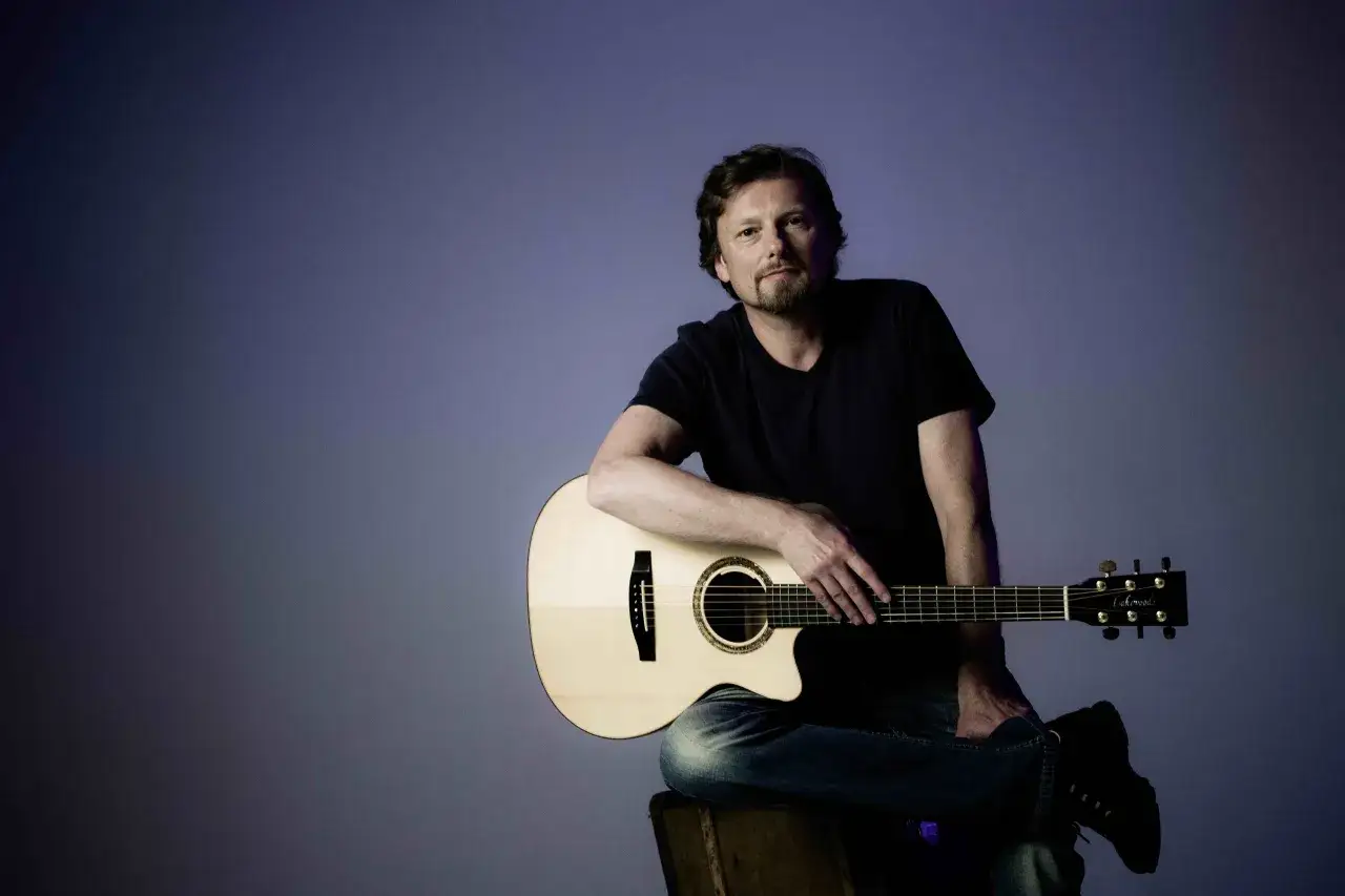 Albert Frey sitzt mit einer Gitarre auf einem alten Koffer.
