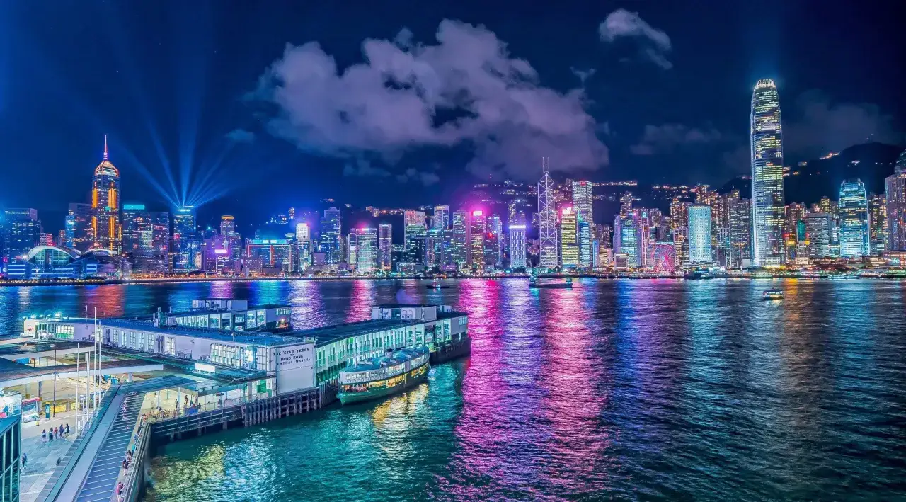 Nocny widok na oświetlone drapacze chmur w Hongkongu, odbijające się w wodzie. Ciekawe fakty o tym mieście można odkrywać, podziwiając tę panoramę.