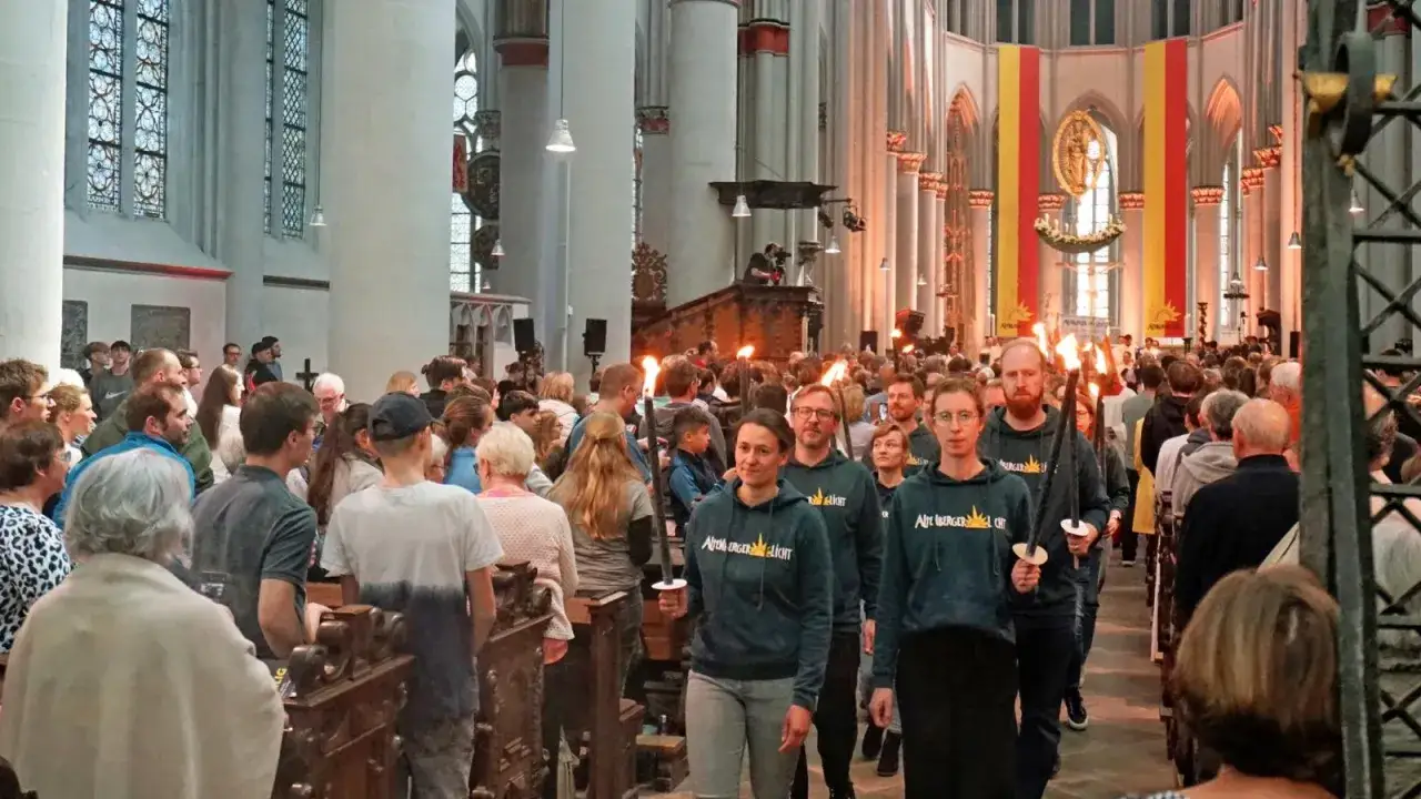Menschen tragen Fackeln in einer Kirche. Das altenberger licht erhellt die Szene, während die Teilnehmer einer Prozession folgen.