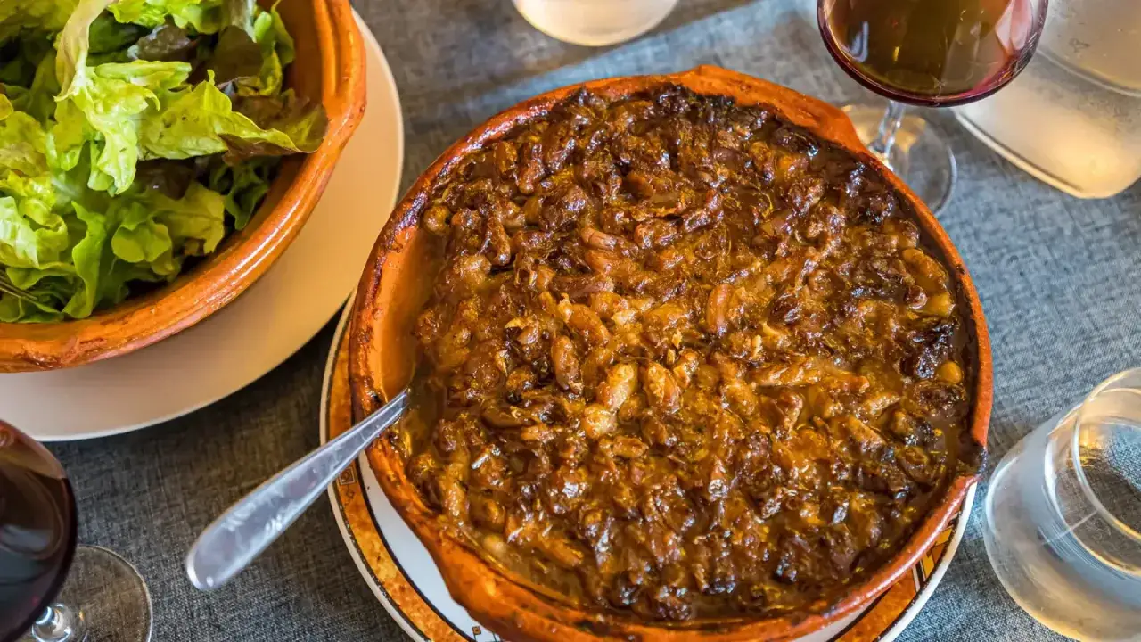 Cassoulet de Castelnaudary reci&eacute;n horneado en cazuela de barro, acompa&ntilde;ado de ensalada verde y vino tinto.