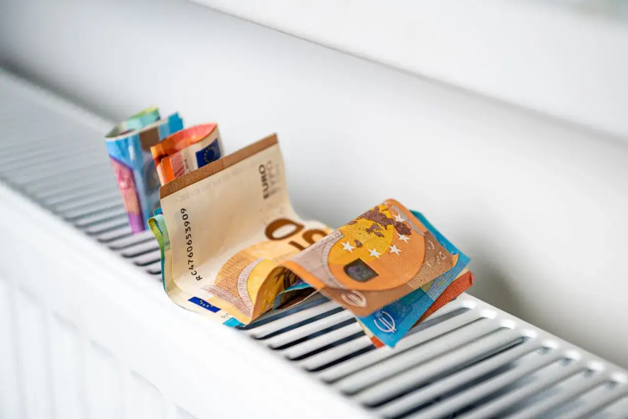 Des billets en euros pliés sur un radiateur, symbolisant le coût élevé du chauffage et la consommation.