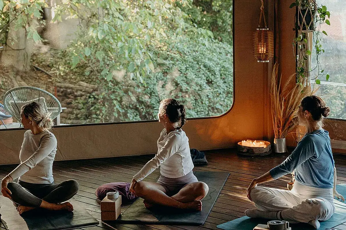 Trois femmes pratiquent le yoga en tailleur, profitant de la lumi&egrave;re naturelle pour calmer son mental.