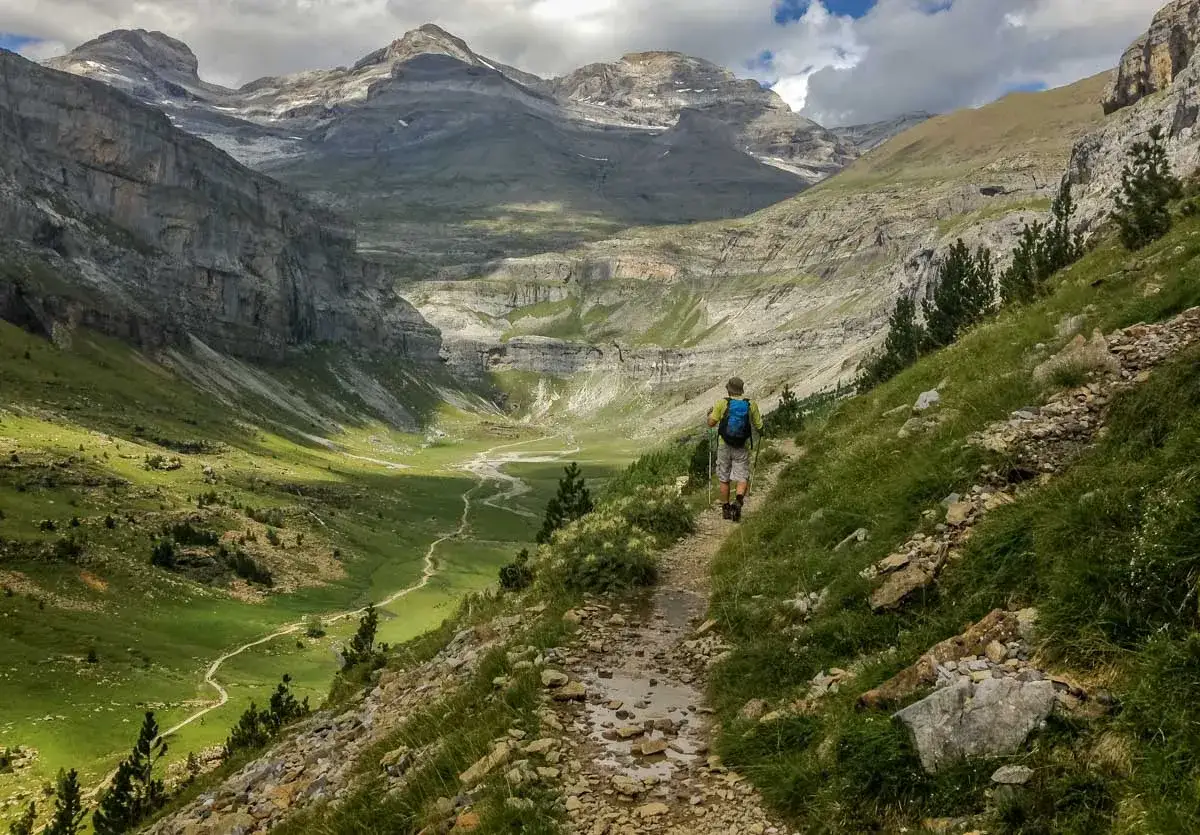 Randonneur explorant la **selva de Oza**, un paysage de montagne spectaculaire avec une vallée verdoyante et un sentier rocailleux.