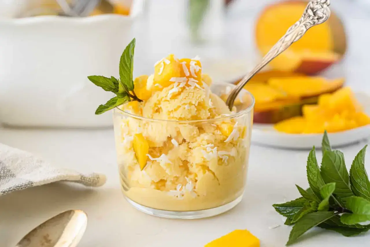 Cremiges Mango Eis mit Kokosraspeln und frischer Minze, garniert mit Mangost&uuml;cken. Ein L&ouml;ffel wartet schon auf den Genuss.