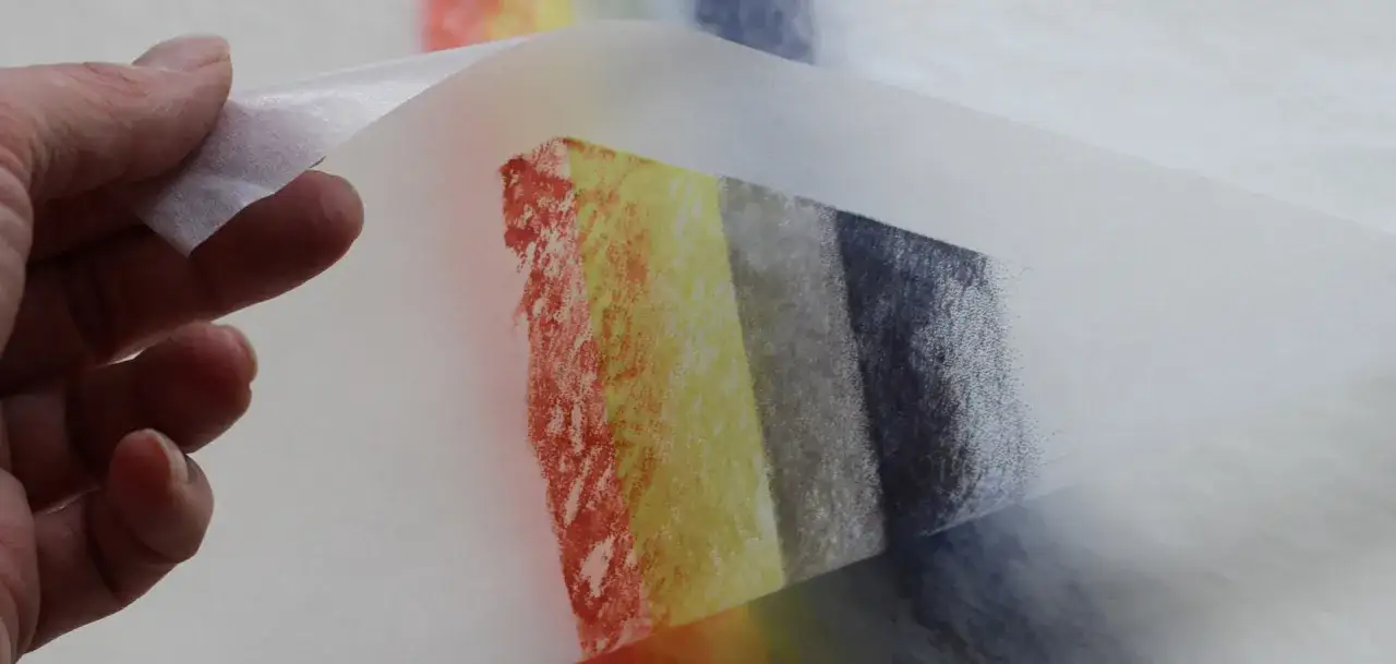 Main d'une personne tenant un papier calque avec des d&eacute;grad&eacute;s de couleurs, du rouge au bleu, comme une &oelig;uvre d'art en taille papier g.