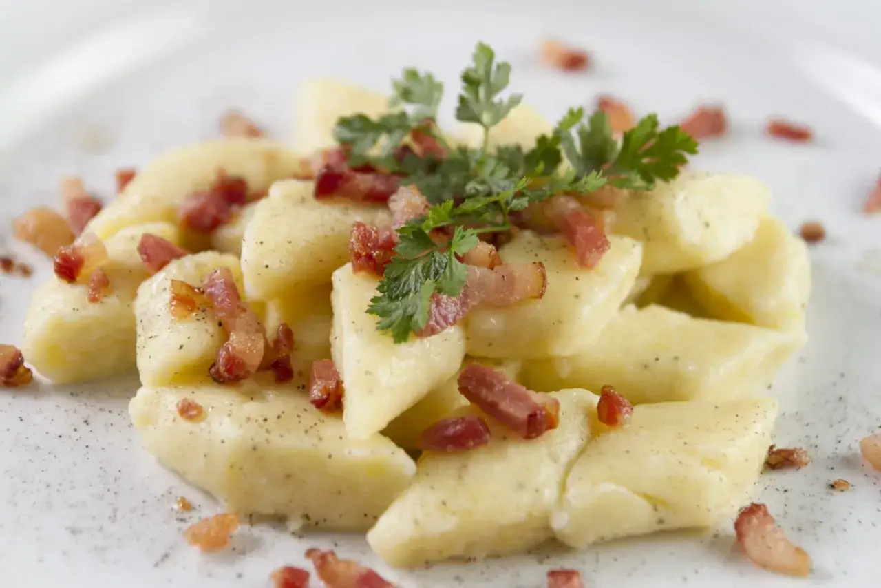Pyszne makaron gnocchi z chrupiącym boczkiem i natką pietruszki na białym talerzu.