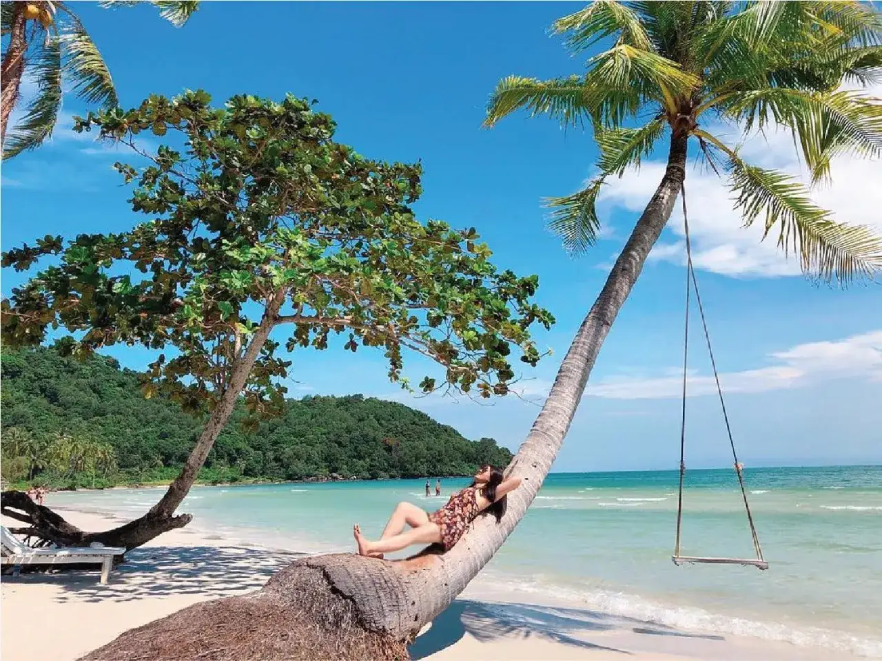 Kobieta odpoczywa na pochyłej palmie na rajskiej plaży Sao Beach. W tle turkusowe morze i zielone wzgórza.