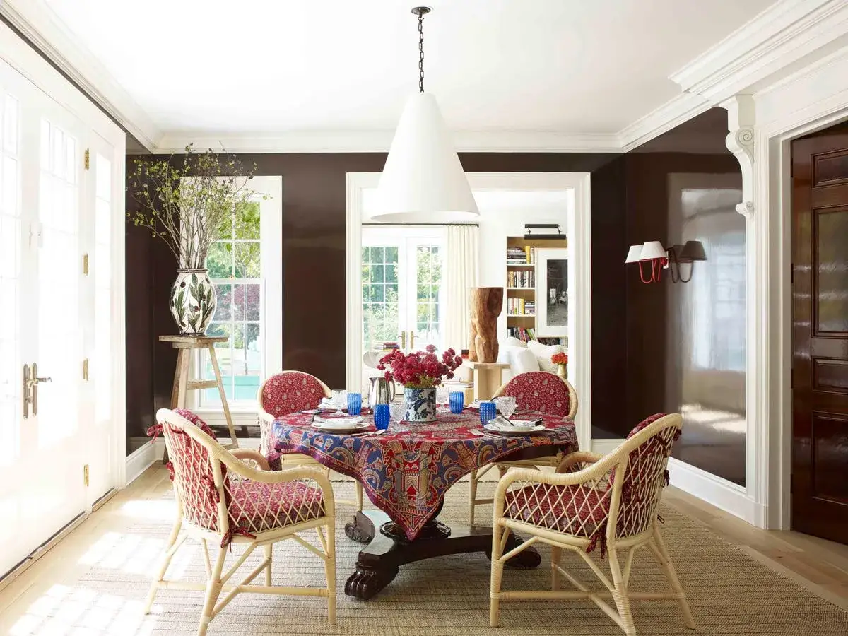 Comedor moderno con mantel estampado, sillas de mimbre y cojines rojos. Inspiraci&oacute;n de colores para un espacio acogedor.