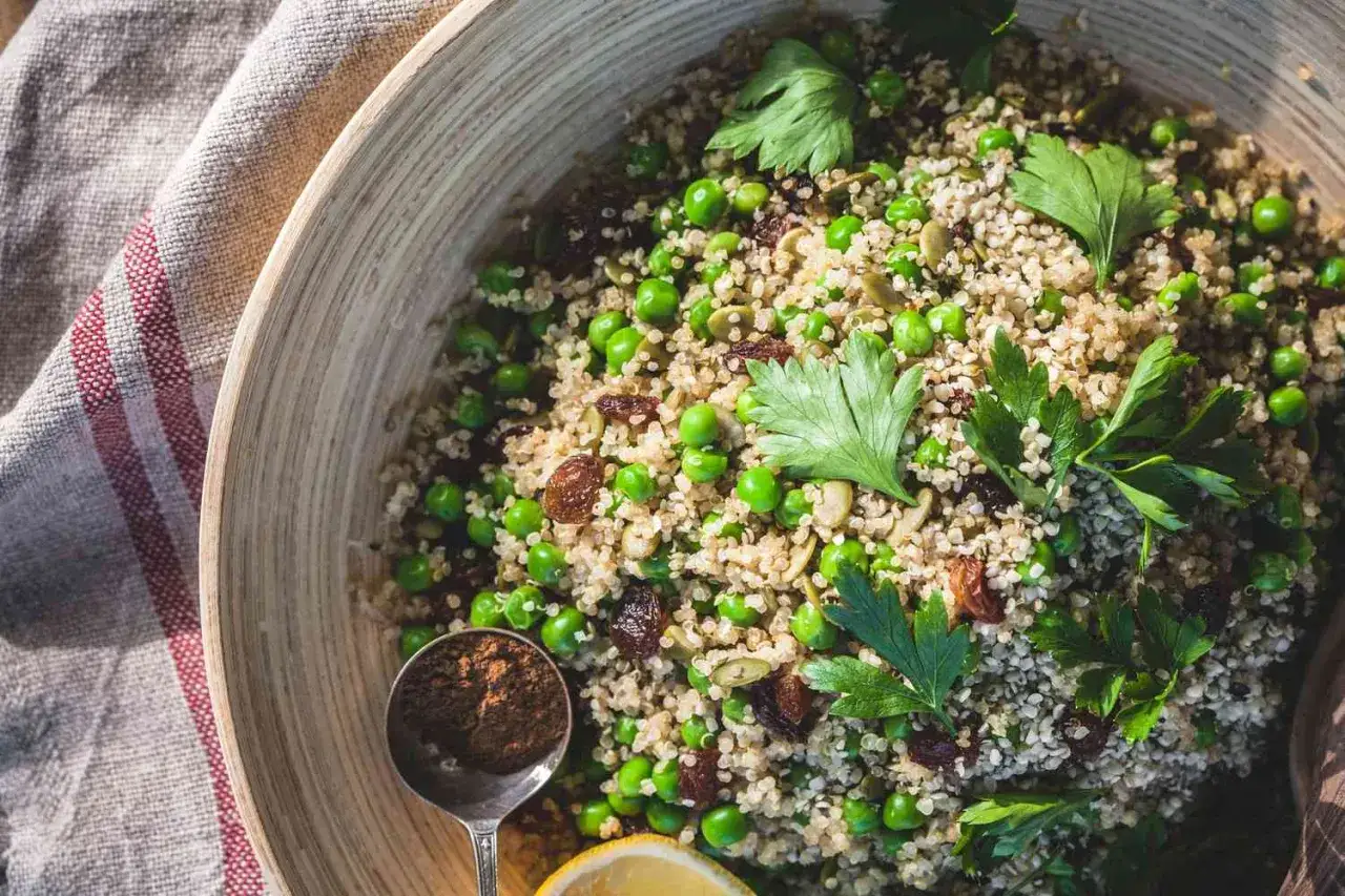 Quinoa quellen lassen ohne kochen: Ein bunter Salat mit Erbsen, Rosinen und K&uuml;rbiskernen in einer Holzschale, garniert mit Petersilie.