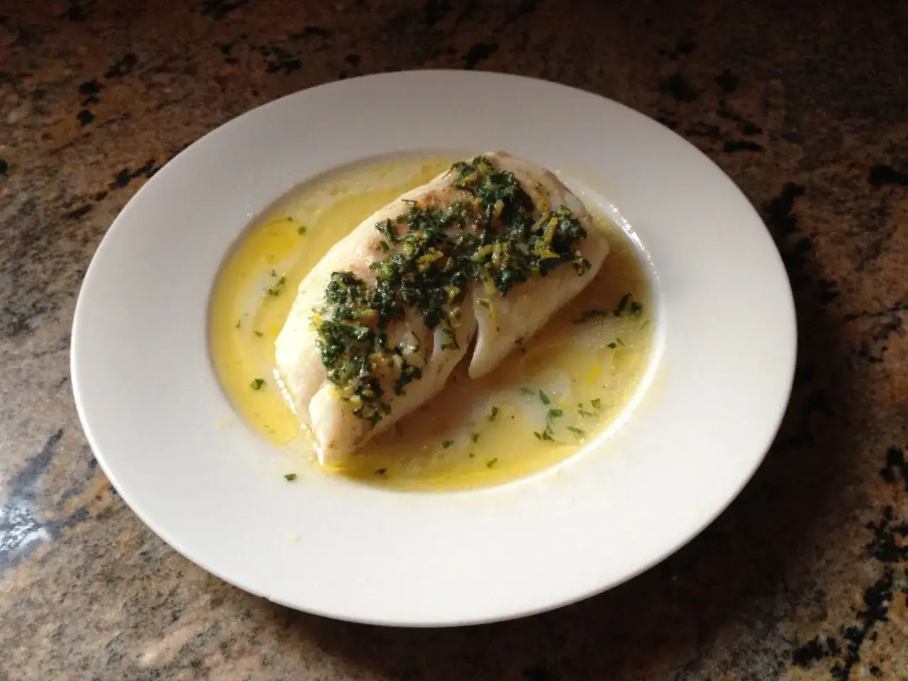 Un d&eacute;licieux poisson en papillote, napp&eacute; d'une sauce citronn&eacute;e et parsem&eacute; d'herbes fra&icirc;ches, servi dans une assiette blanche.