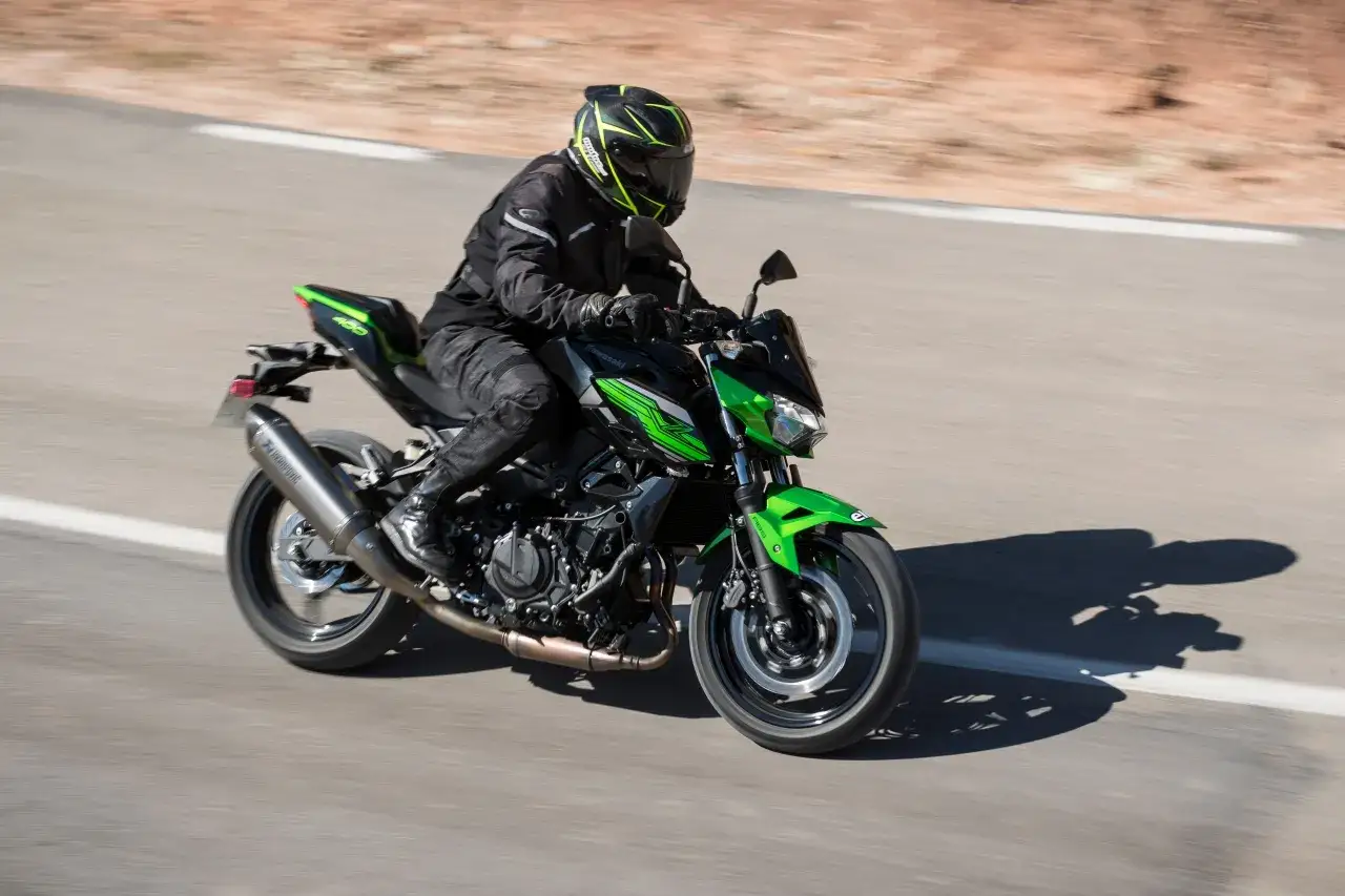 Motociclista con casco verde y negro conduce una Kawasaki Z400 cv negra y verde por una carretera.
