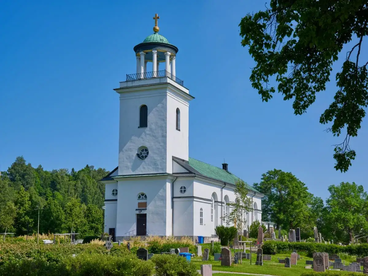 Vitt kyrktorn med grönt tak under en klarblå himmel, en vacker syn på Kristi himmelsfärdsdag. Kyrkogården är grönskande.