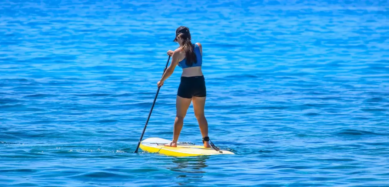 Eine Frau steht auf einem gelben Board und paddelt auf dem blauen Meer. Sie genie&szlig;t das sub fahren.