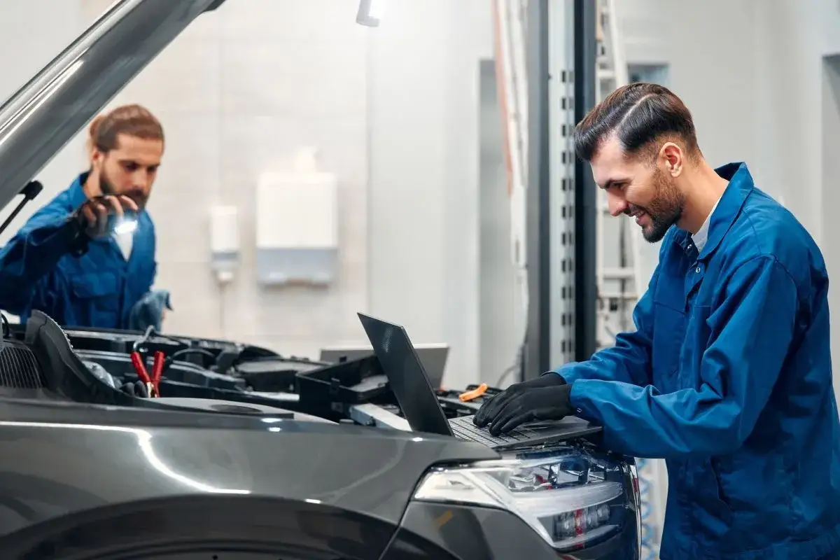 Mechanik diagnozuje drgania silnika, analizując dane na laptopie, podczas gdy kolega oświetla komorę silnika latarką.