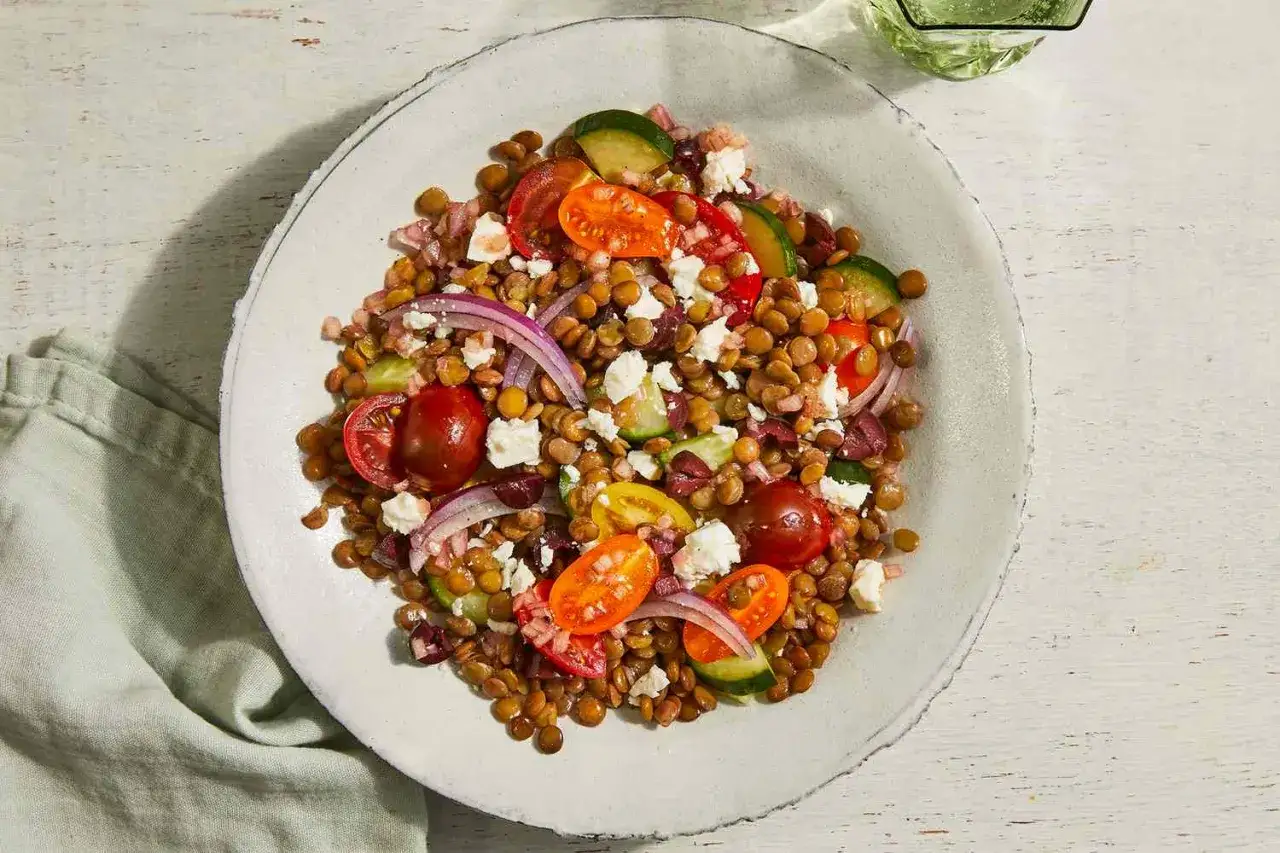 Ein bunter Linsensalat mit Feta, Kirschtomaten, Gurken und roten Zwiebeln, serviert auf einem rustikalen Teller.