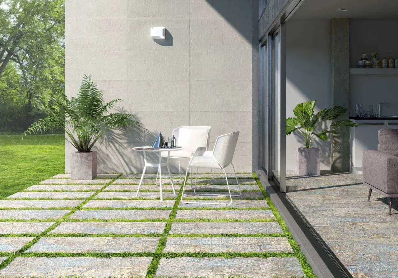 Modernos suelos para patios interiores con un diseño de baldosas y césped. Una mesa y sillas blancas invitan a relajarse al aire libre.