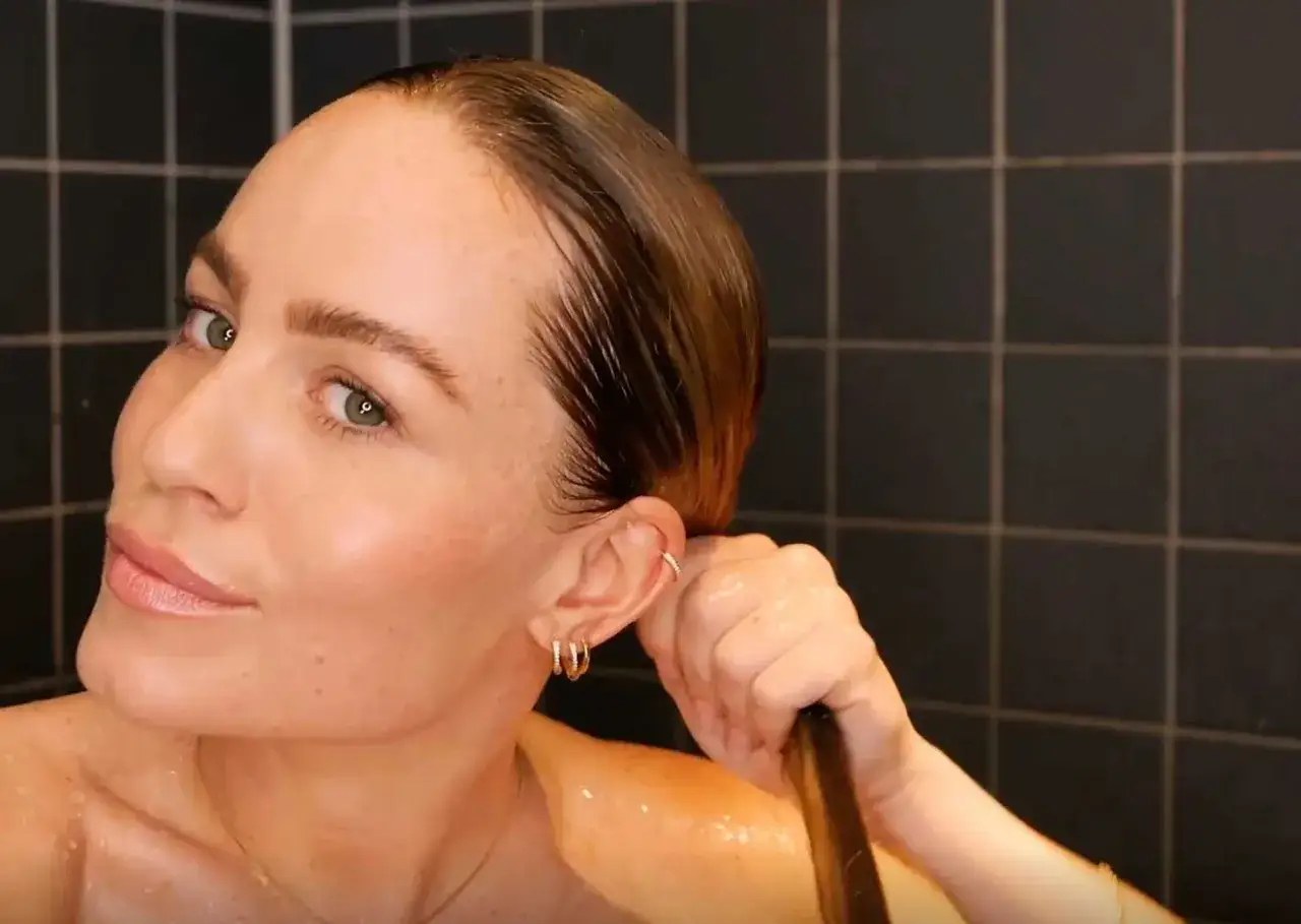 Kvinna i duschen, med blött hår och smycken, som utför co-washing för mjukt och glansigt hår.