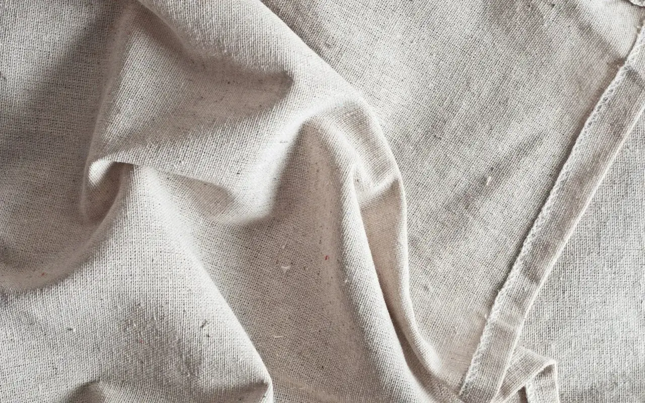 Tessuto grezzo, beige, con pieghe morbide. Scopri come ammorbidire un tessuto sintetico per un tocco più piacevole.