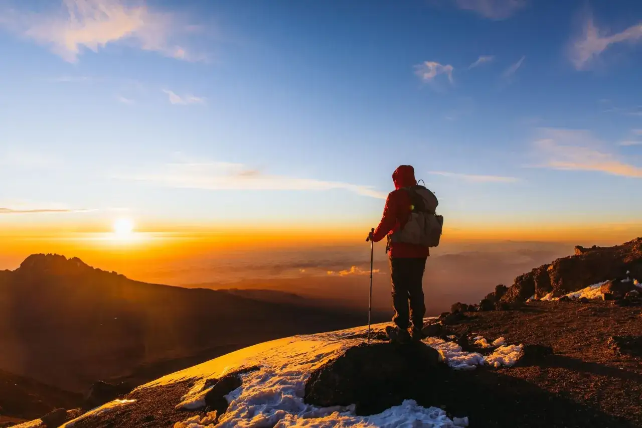 Vandrare p&aring; toppen av Kilimanjaro vid soluppg&aring;ngen, en dr&ouml;m om att bestiga Kilimanjaro blir verklighet.