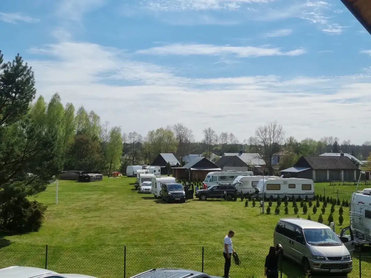 Urokliwy **camping Roztocze** z przyczepami kempingowymi i kamperami na zielonej trawie, pod błękitnym niebem z chmurami.