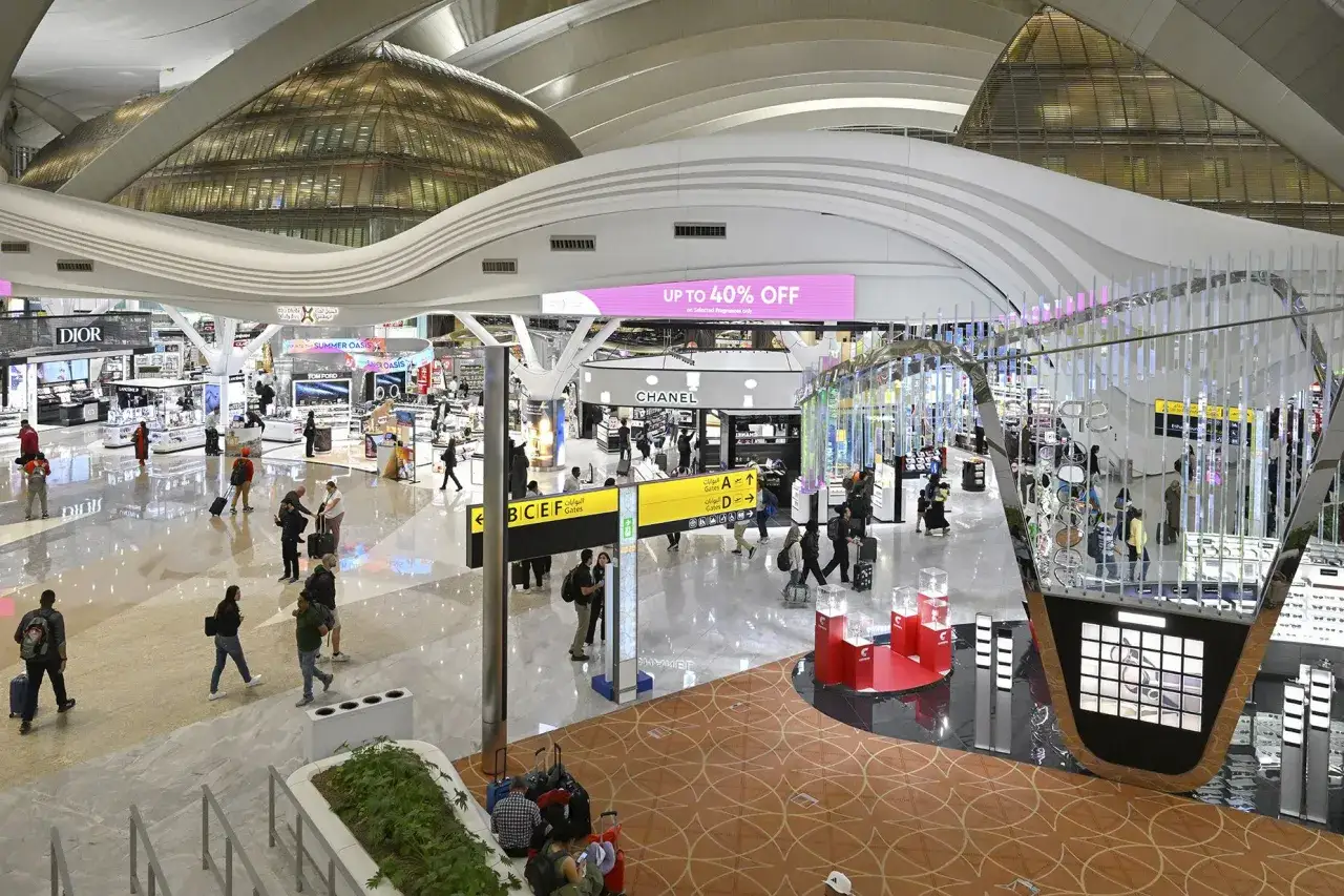 Wnętrze lotniska AUH Zayed International z pasażerami, sklepami i futurystyczną architekturą.
