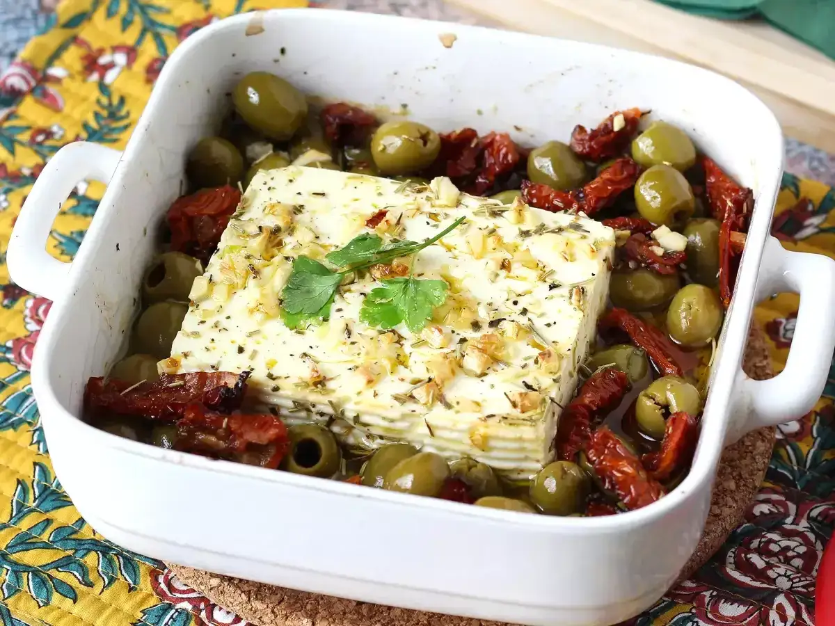 Un bloc de feta cuit au four, entouré d'olives vertes et de tomates séchées. Une recette simple et savoureuse avec feta.