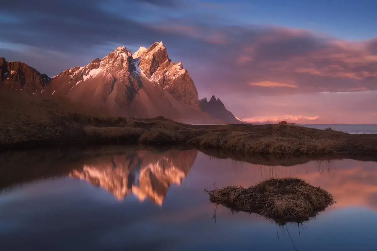 A majestic mountain range, kissed by sunset light, is reflected in a still lake. This great depth of field photography captures the serene beauty of the Icelandic landscape.