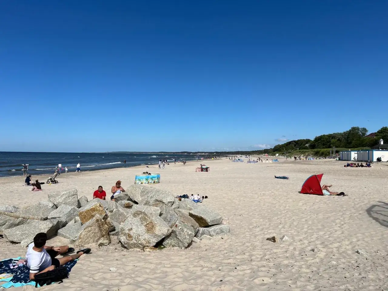 Słoneczna plaża w Ustce i okolicy. Warto zobaczyć to miejsce pełne wypoczywających ludzi, z widokiem na morze i zielone wzgórza.