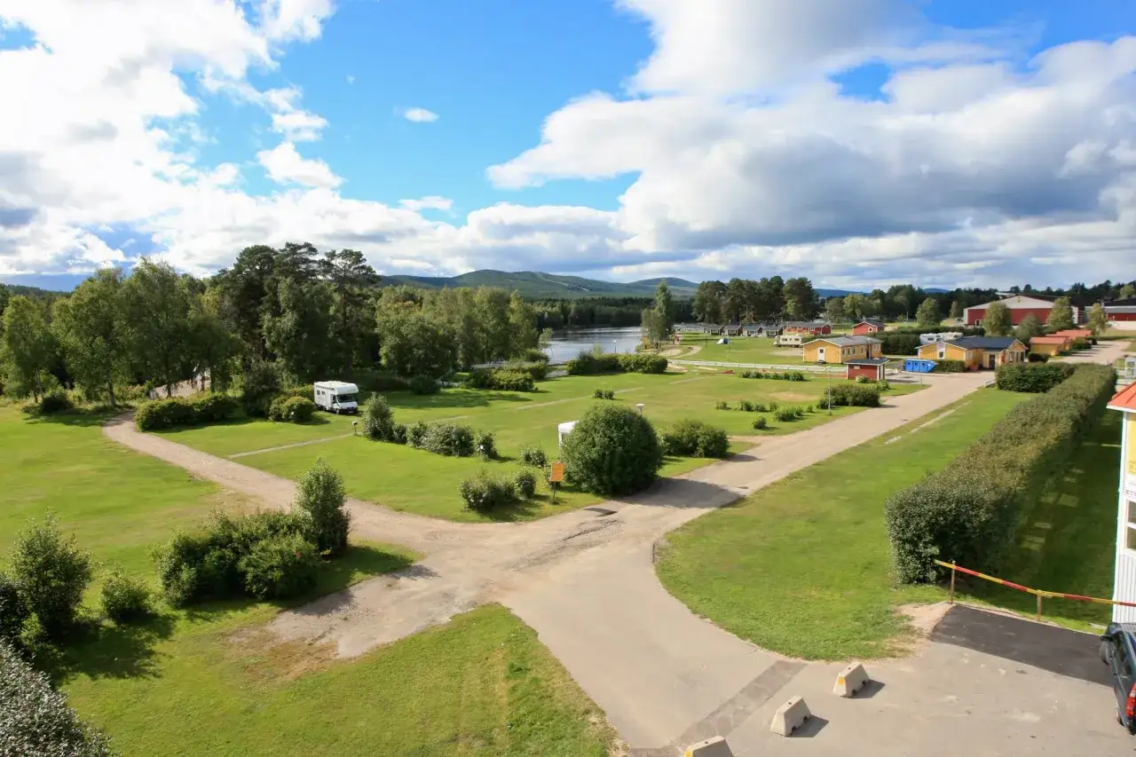 Vacker vy över svegs camping med husbilar, stugor och en sjö i bakgrunden under en molnig men solig dag.