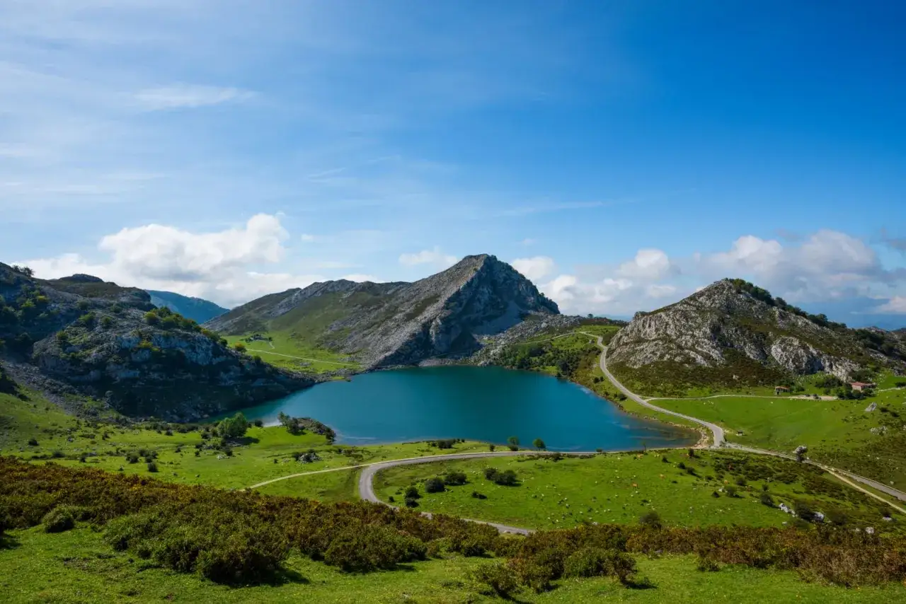 Un lago azul rodeado de monta&ntilde;as verdes y caminos sinuosos, un ejemplo perfecto de qu&eacute; es un parque nacional, con cielos despejados y nubes dispersas.