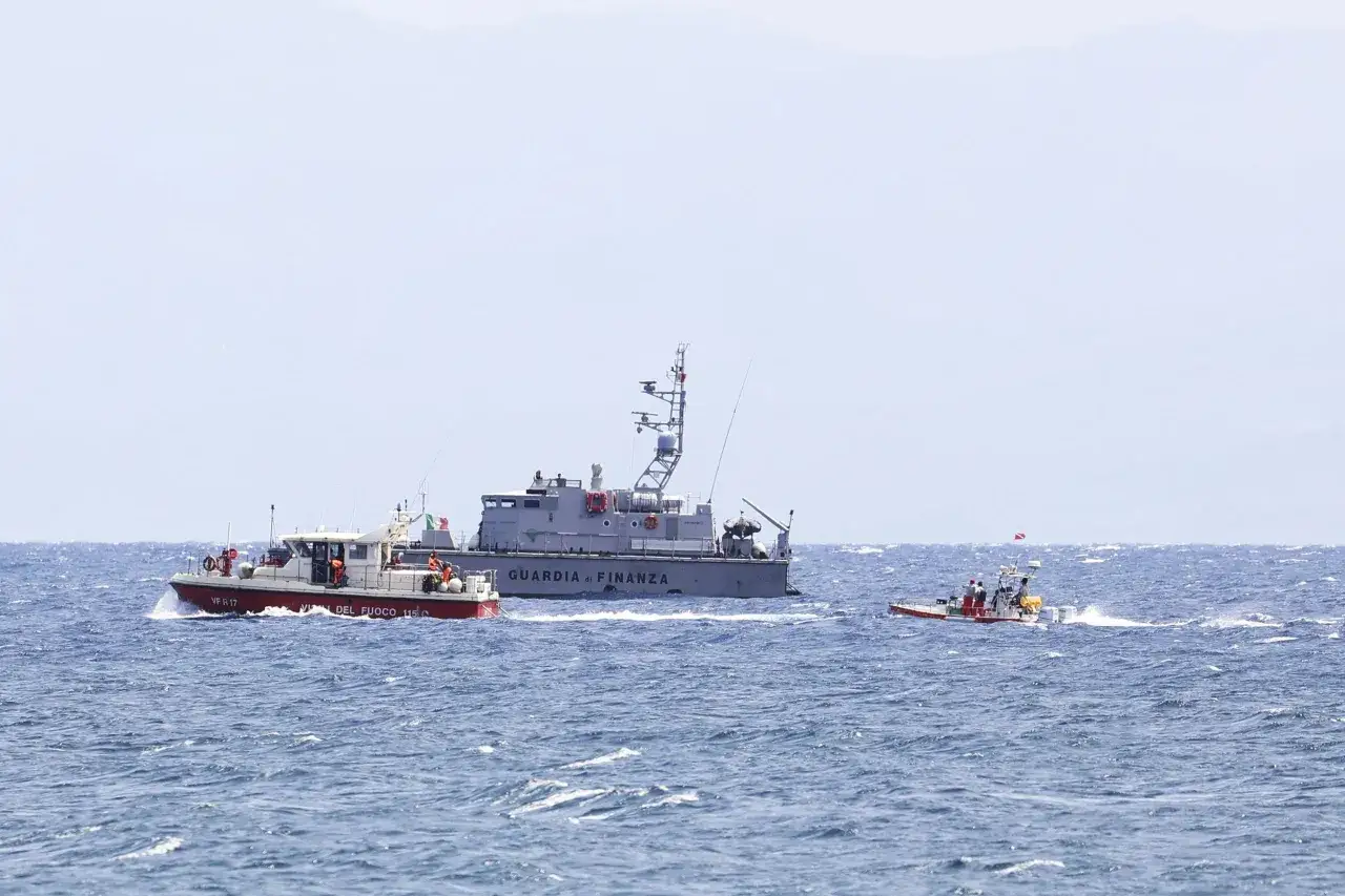 Trois bateaux, dont un navire de la Guardia di Finanza et un bateau de pompiers, naviguent sur une mer agitée. Un petit bateau de sauvetage, tel un bayesian yacht, se tient à l'écart.