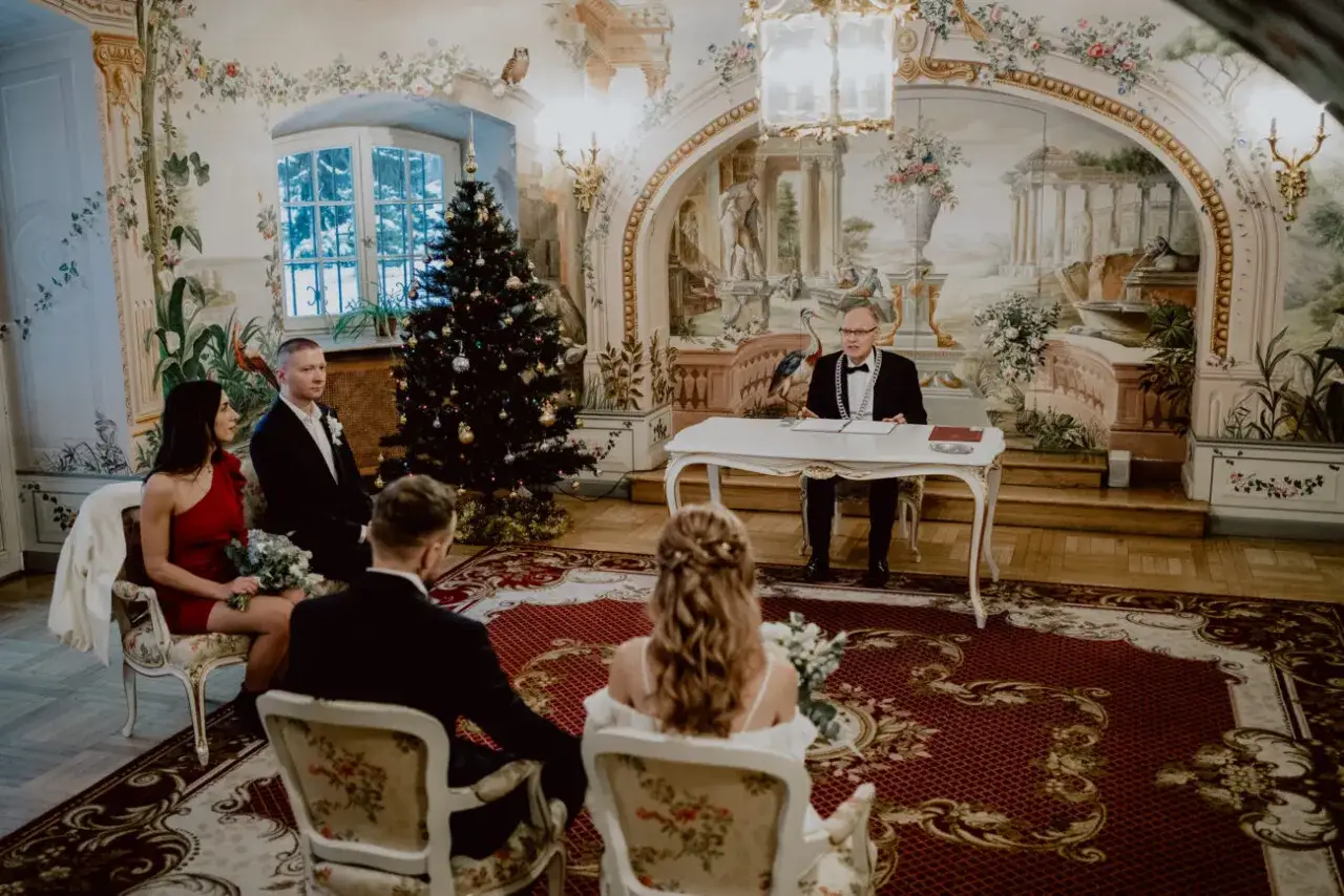 Ślub w świątecznej sali. Urzędnik czeka na podpis, czy świadek musi być pełnoletni? Para młoda siedzi przed nim.