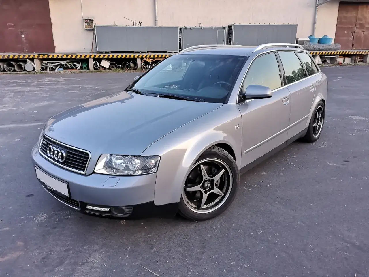 Srebrne Audi A4 B6 1.9 TDI Avant na felgach z czarnymi ramionami, zaparkowane na placu przemysłowym.