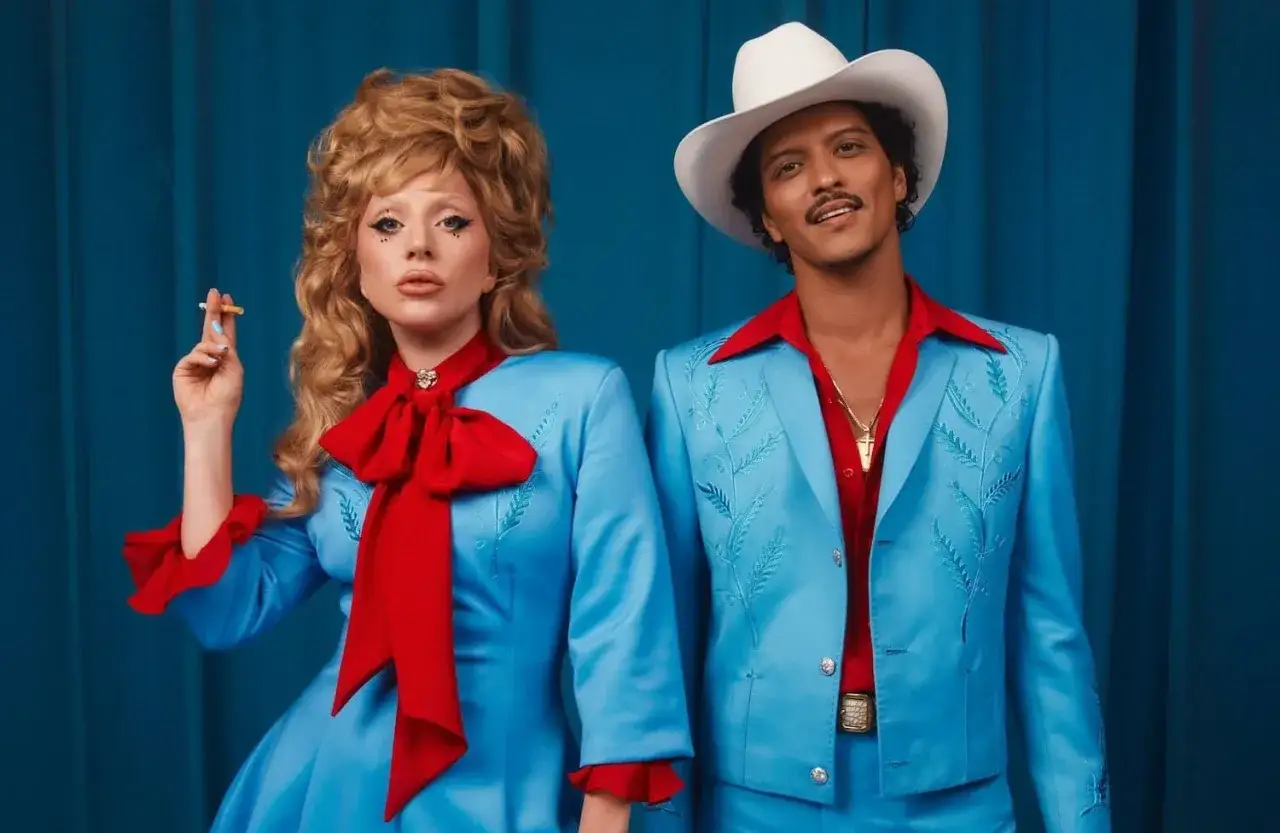 Lady Gaga i Bruno Mars w błękitnych strojach z czerwonymi akcentami. Ona pali papierosa, on w białym kapeluszu. Tekst
