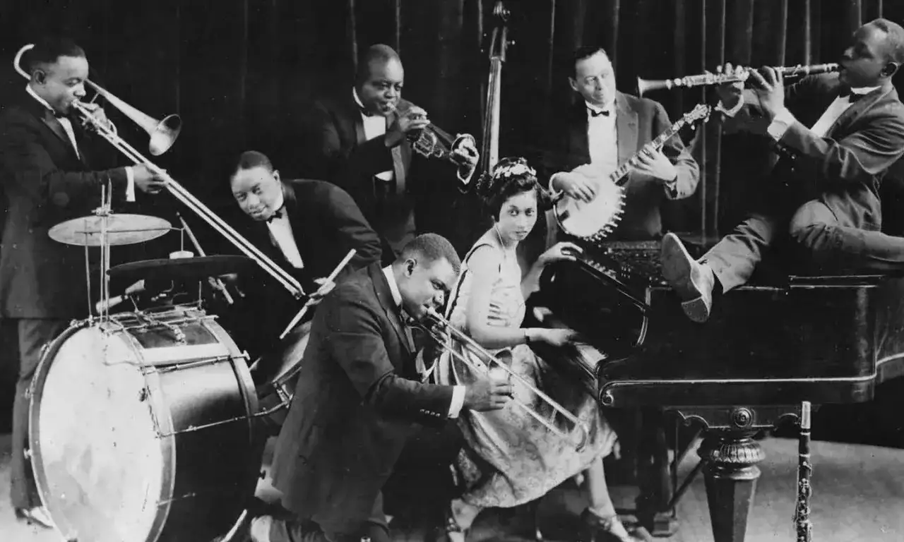 Zespół grający jazz, uchwycony w klasycznym stylu. Widać instrumenty dęte, banjo, pianino i perkusję.