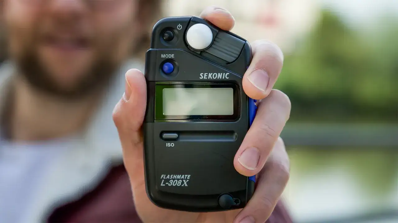 Dłoń trzyma czarny światłomierz Sekonic Flashmate L-308X.