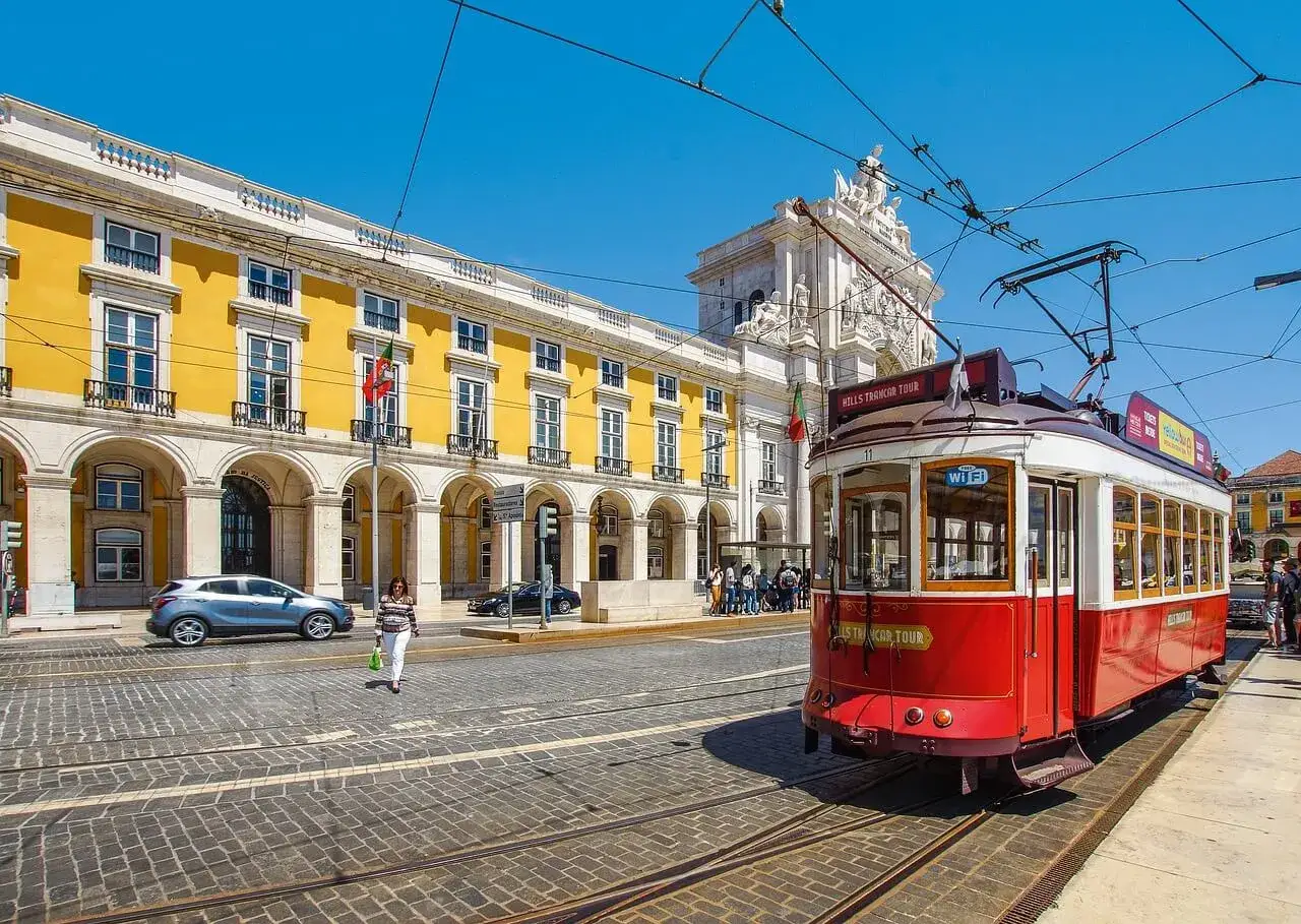 Czerwony tramwaj w Lizbonie, obok żółtego budynku z arkadami. Czy do Portugalii potrzebny jest paszport? Tak, jeśli nie jesteś obywatelem UE.