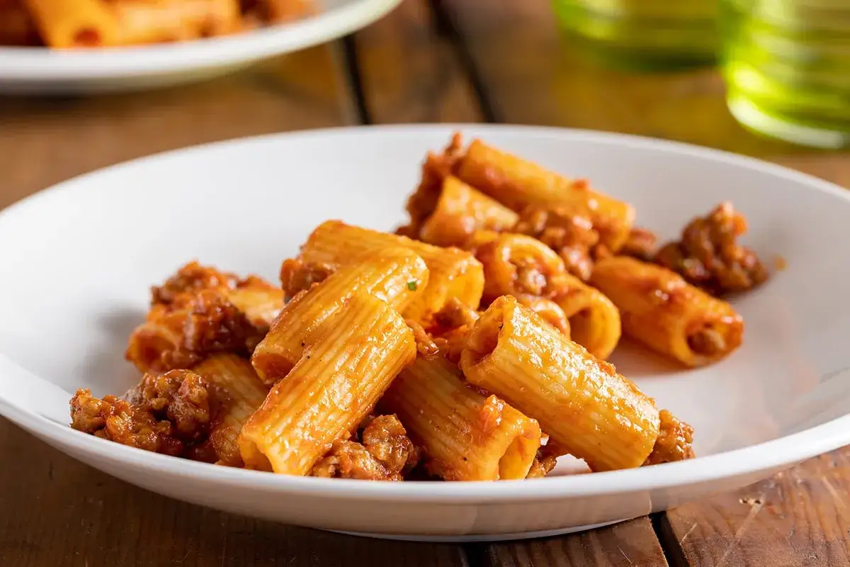 Rigatoni conditi con un ricco ragù di salsiccia alla napoletana, serviti su un piatto bianco.