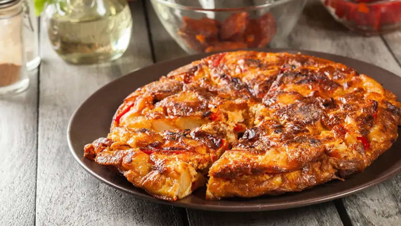 Tortilla de chorizo, patatas y pimientos, dorada y jugosa, servida en plato marrón sobre mesa de madera.