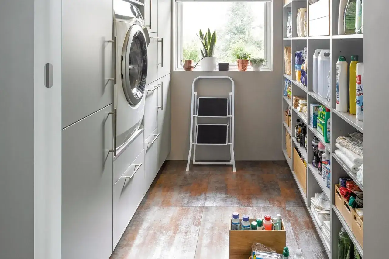 Ordnung im kleinen Hauswirtschaftsraum: Waschmaschine, Schr&auml;nke, Regale voller Reinigungsmittel und eine Trittleiter.