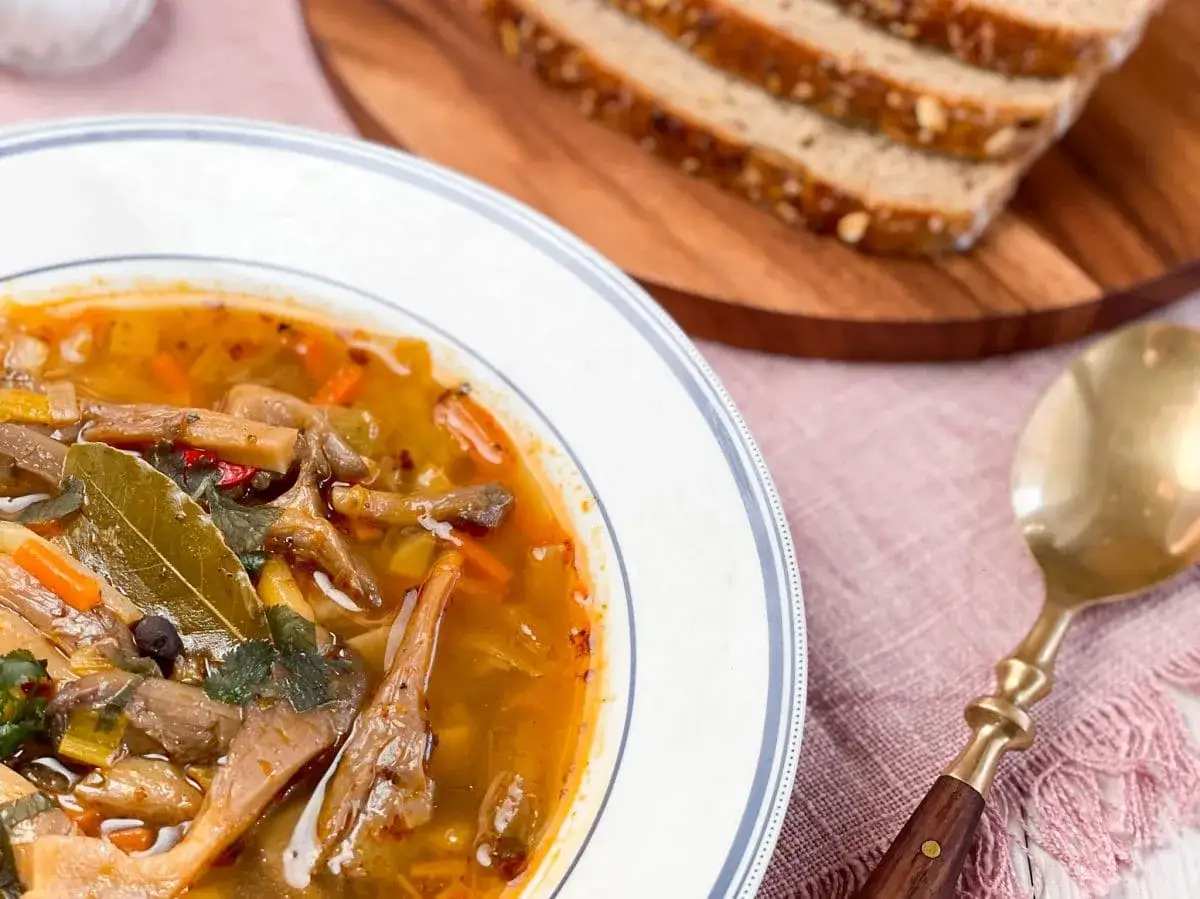 Aromaticzne flaki z boczniak&oacute;w w głębokim talerzu, obok kromki chleba i złotej łyżki. Pyszne danie wegetariańskie.