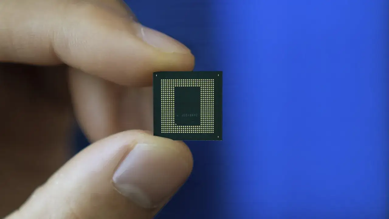 Palec trzyma mały, kwadratowy układ scalony z rzędem złotych pin&oacute;w. To serce smartfona, procesor Snapdragon.