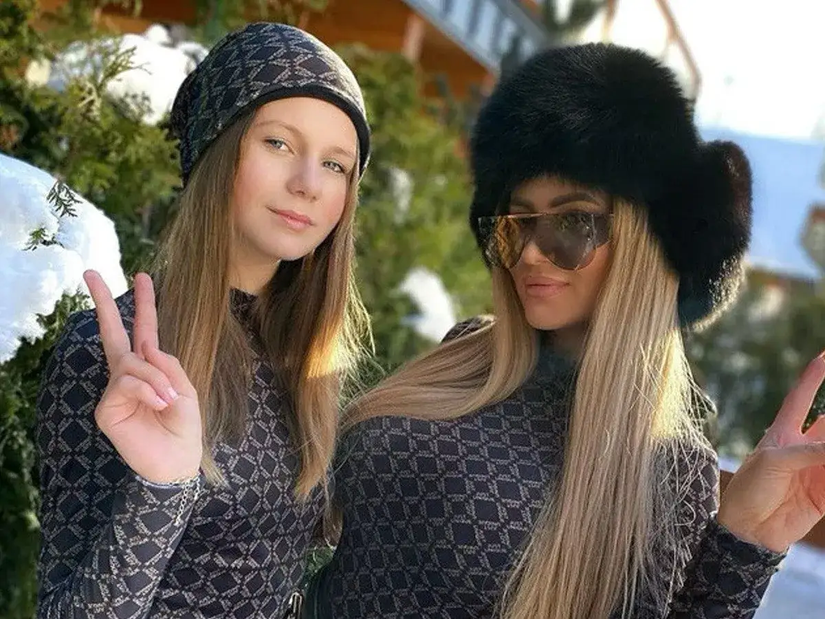 Dwie kobiety w zimowych stylizacjach pozdrawiają, jedna z nich to Eliza Macudzińska. Wiek nie jest widoczny, ale obie wyglądają na szczęśliwe.
