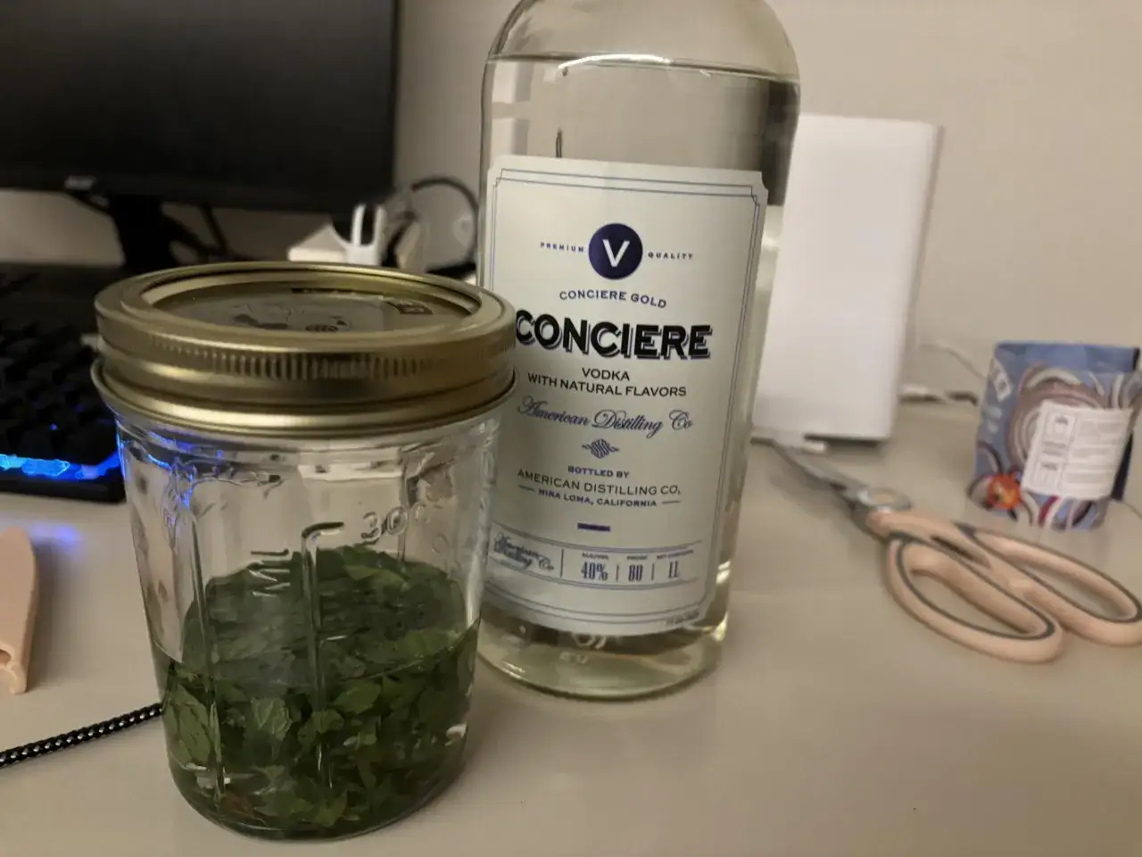 Słoik z miętą i butelka wódki - składniki do domowego zielonego likieru miętowego typu creme de menthe.