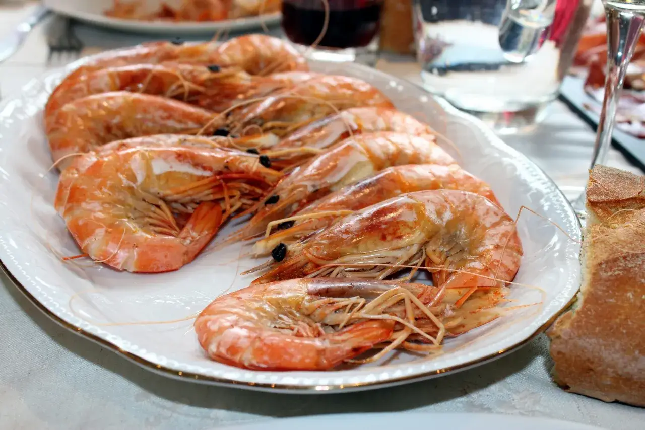Plato blanco con langostinos cocidos, perfecto para recetas con langostinos. Acompañado de pan y vino tinto.