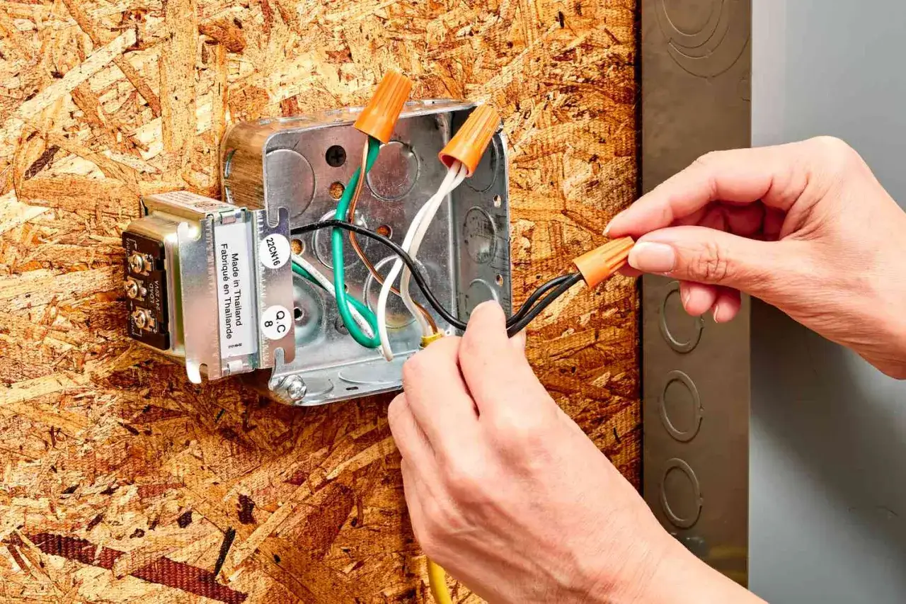 Manos conectando cables con capuchones naranjas a un transformador, parte de como arreglar el timbre de la puerta.