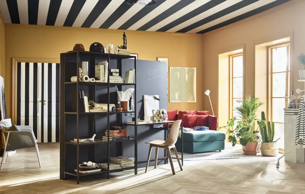 Un salon moderne avec un tableau cactus, des étagères noires, un canapé rouge et des plantes vertes.